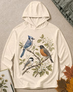 Women's light yellow sun hoodie with a blue jay and robin on flowering branches, front view.
