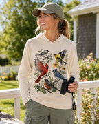Woman wearing a light yellow sun hoodie with cardinals, blue jays, goldfinches and flowers outdoors.