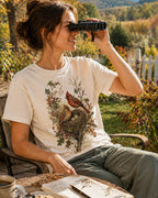 Woman wearing a off white cotton T-shirt with a cardinal pair beside a nest outdoors.
