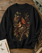 Women's black crewneck sweatshirt with a cardinal pair beside a nest, front view.