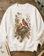 Women's white crewneck sweatshirt with a cardinal pair beside a nest, front view.