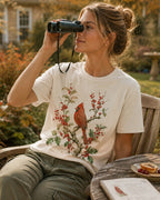 Woman wearing a off white cotton T-shirt with a cardinal among red berry branches outdoors.