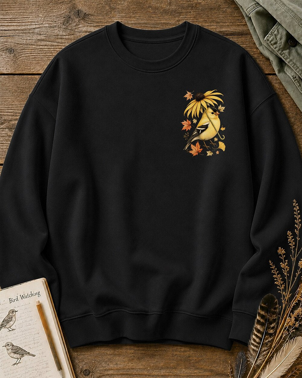 Women's black crewneck sweatshirt with a small goldfinch and flower chest print, front view.