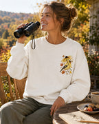 Woman wearing a white crewneck sweatshirt with a small goldfinch and flower chest print outdoors.