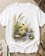 Women's white cotton T-shirt with a goldfinch beside a rocky waterfall, front view.