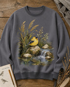 Women's gray crewneck sweatshirt with a goldfinch beside a rocky waterfall, front view.