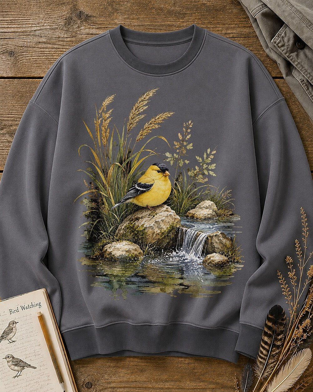Women's gray crewneck sweatshirt with a goldfinch beside a rocky waterfall, front view.
