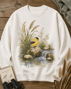 Women's white crewneck sweatshirt with a goldfinch beside a rocky waterfall, front view.