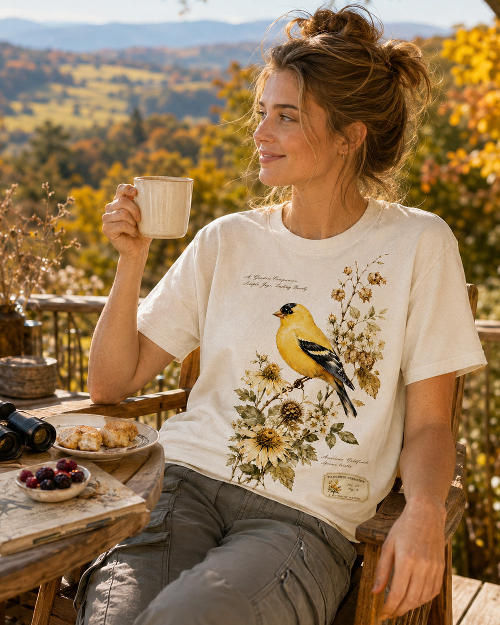 Woman wearing a off white cotton T-shirt with a goldfinch among yellow flowers outdoors.