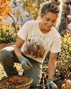 Woman wearing a off white cotton T-shirt with a watering can, pumpkins and harvest flowers outdoors.