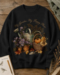 Women's black crewneck sweatshirt with a watering can, pumpkins and harvest flowers, front view.