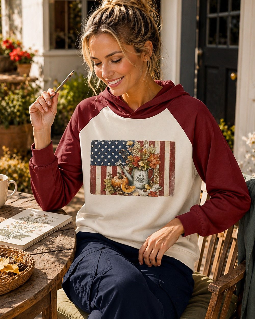 Woman seated in a garden wearing a red and cream sun hoodie with an American flag and autumn garden print.