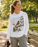 Woman wearing a white sun hoodie with a robin, blossoms and musical notes outdoors.