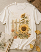 Women's off white cotton T-shirt with sunflowers beside a picket fence, front view.
