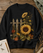Women's black crewneck sweatshirt with sunflowers beside a picket fence, front view.