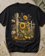 Women's black cotton T-shirt with sunflowers beside a rustic wooden fence, front view.