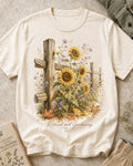 Women's off white cotton T-shirt with sunflowers beside a rustic wooden fence, front view.