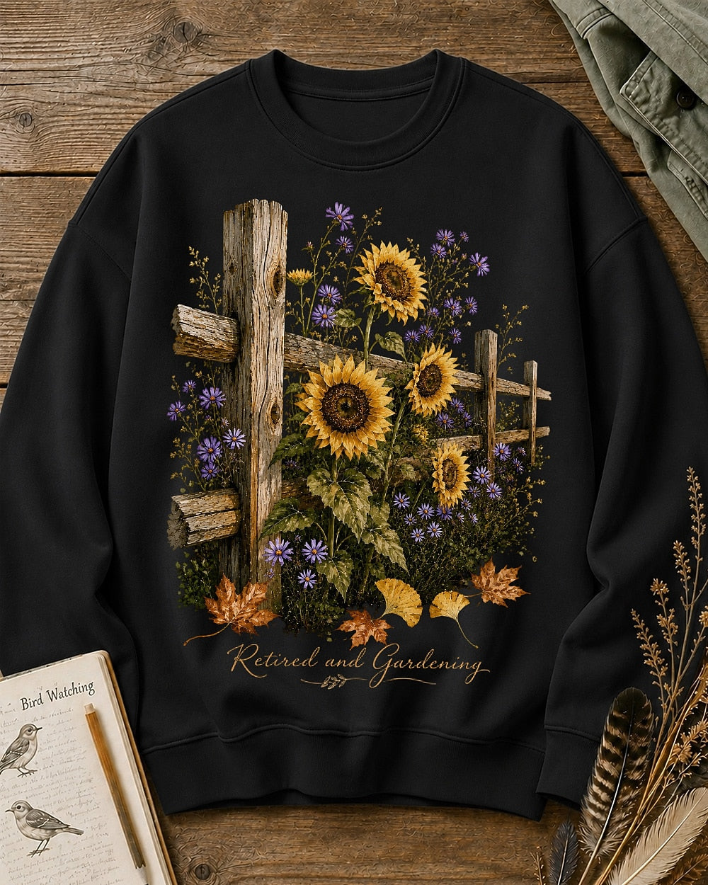 Women's black crewneck sweatshirt with sunflowers beside a rustic wooden fence, front view.